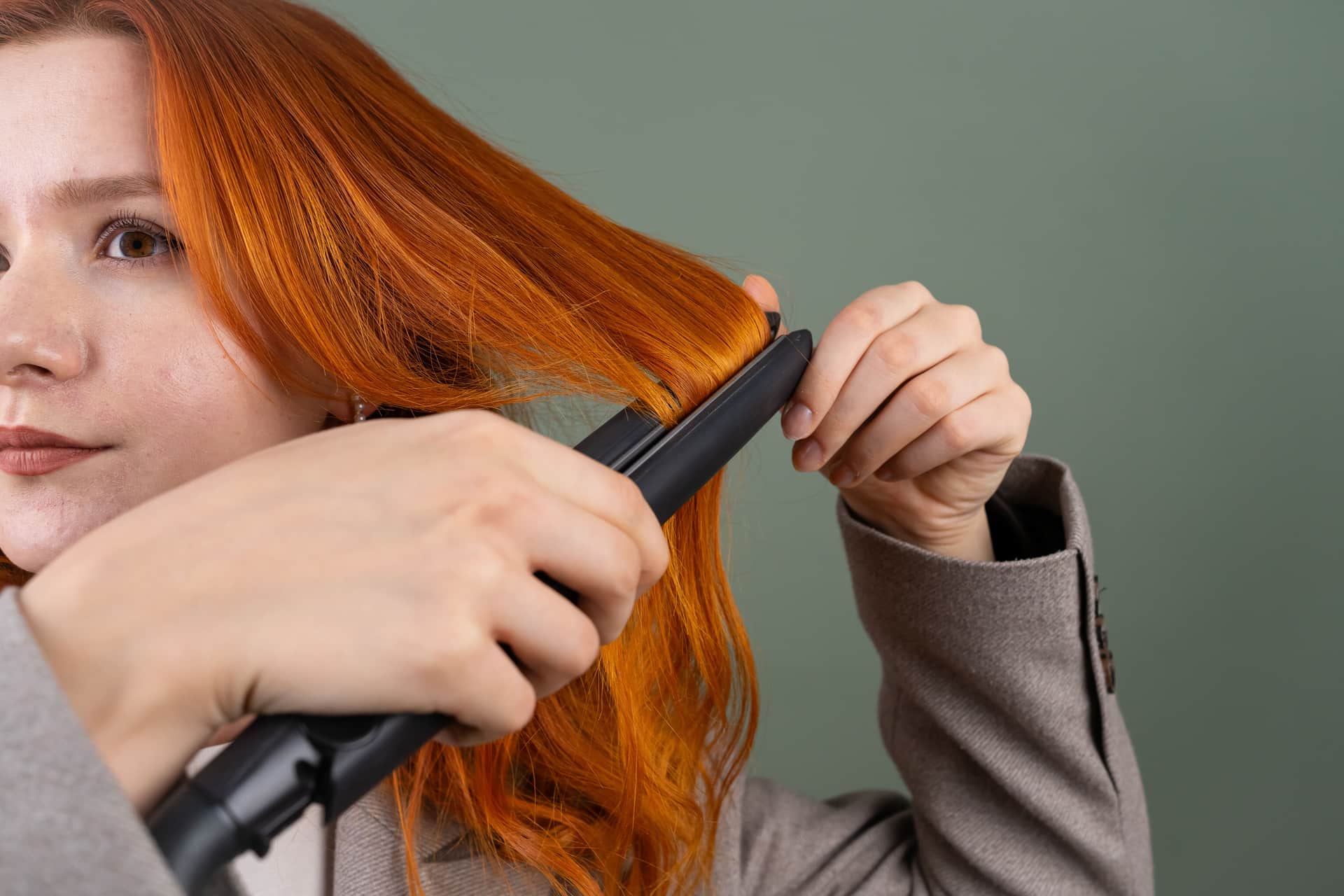 A flat iron passing through a section of straight hair in soft daylight