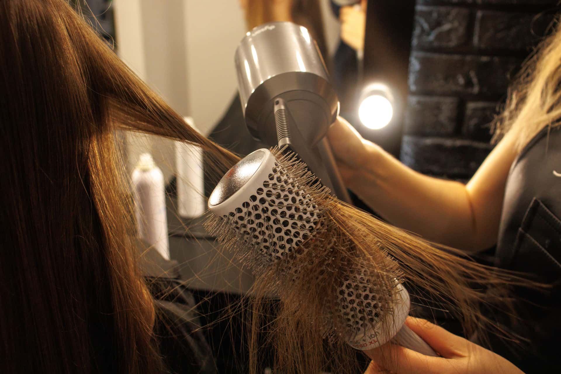 A person drying and shaping hair with a round brush and air styler